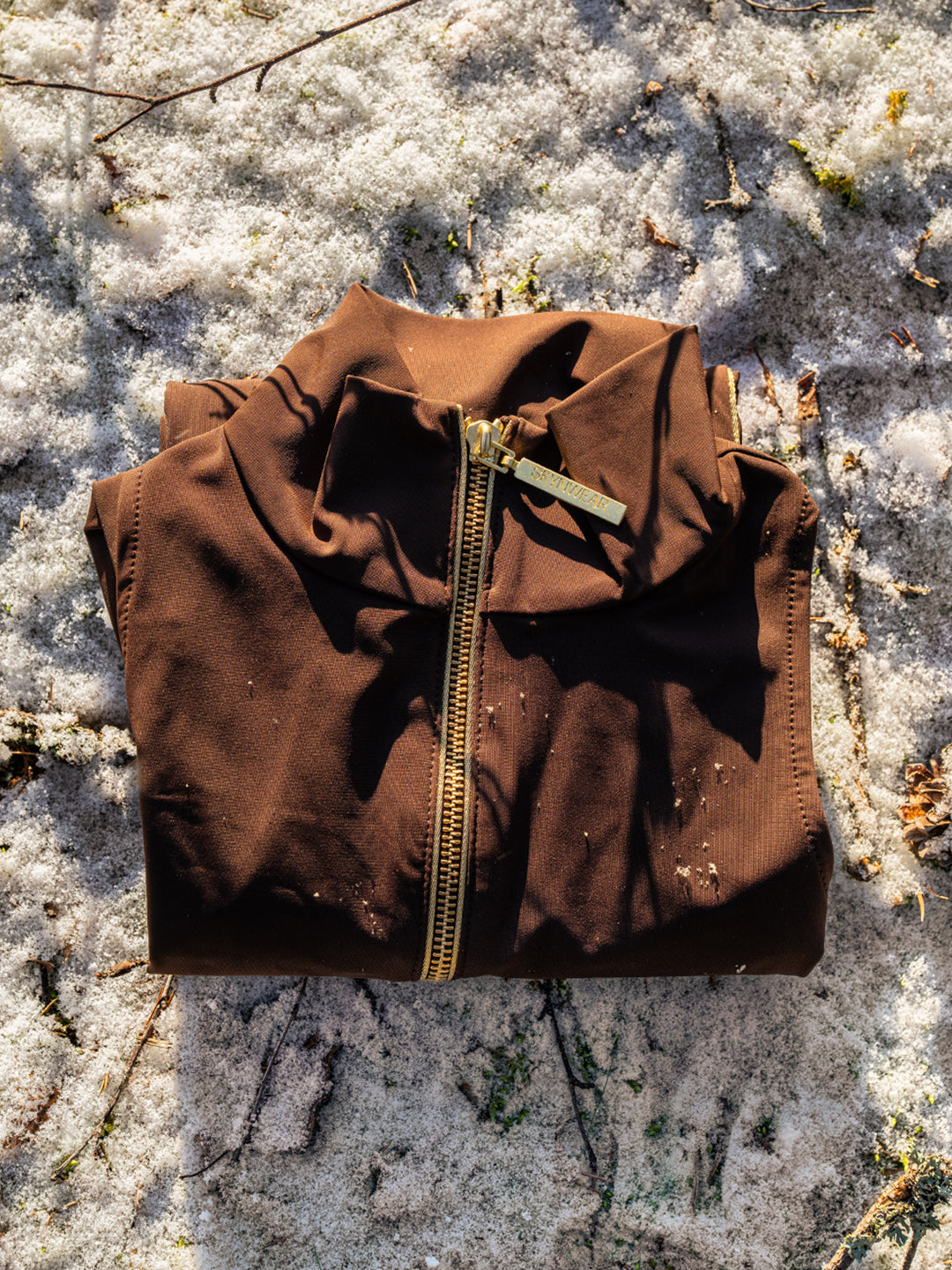 A Skynwear suit in chocolate, folded on fresh snow