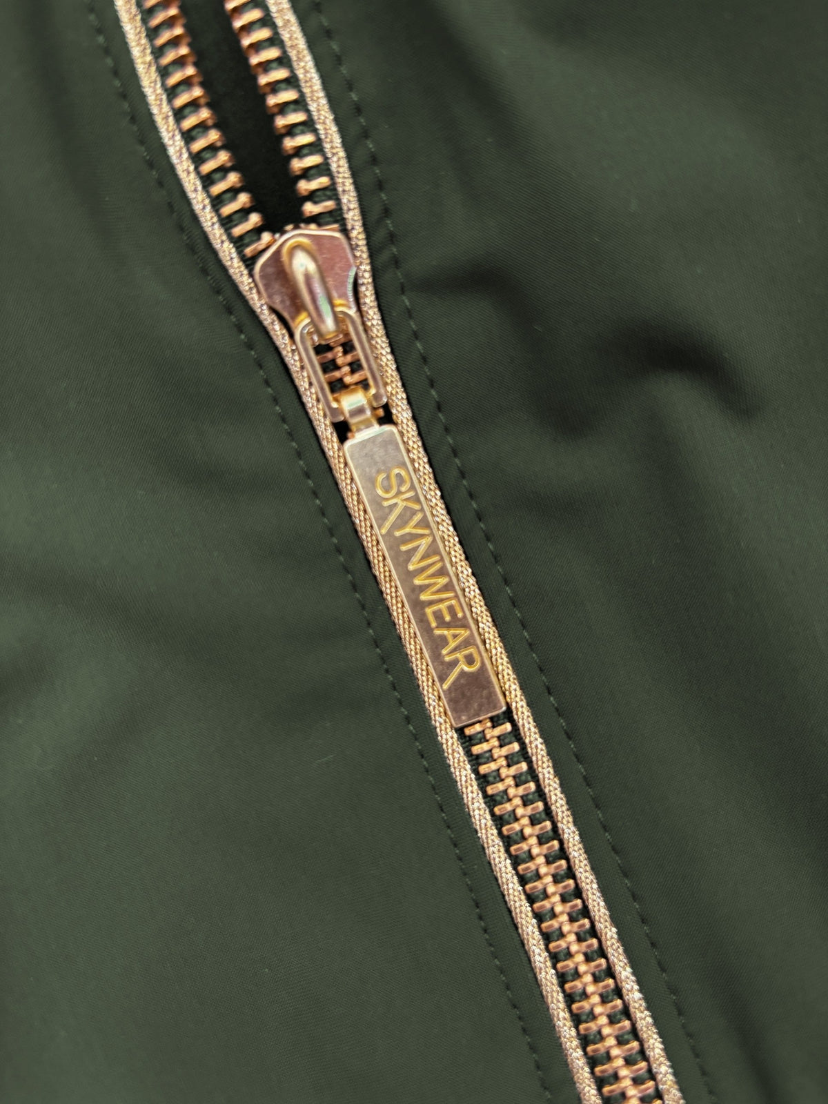 Apex Jumpsuit in khaki, close-up of the gold Skynwear engraved zip